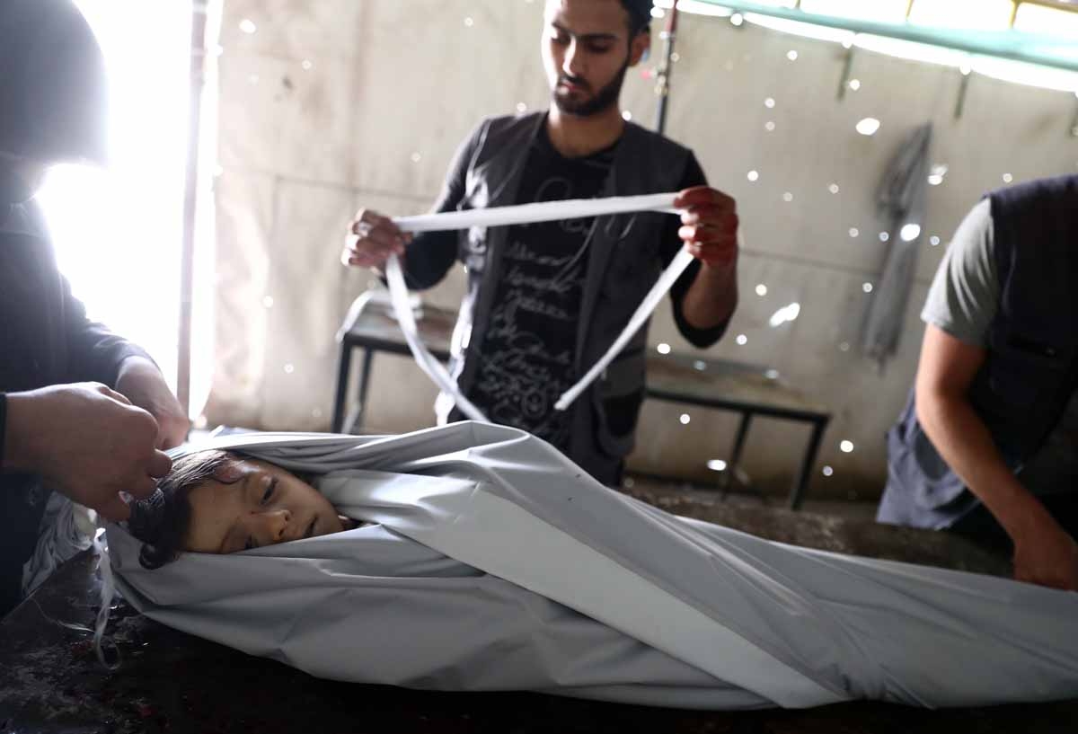 Volunteers wrap in shrouds the body of a Syrian child, Emad, 5, at a makeshift morgue following a reported air stike on the rebel-held town of Douma, east of the capital Damascus, on August 23, 2016. 